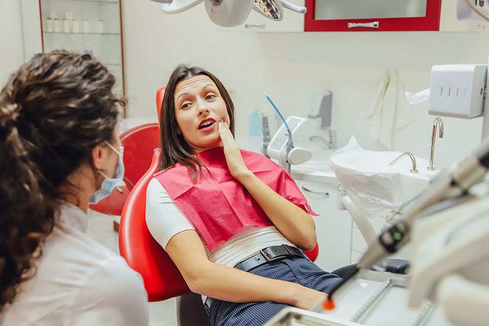 woman in dental chair holding her jaw in pain