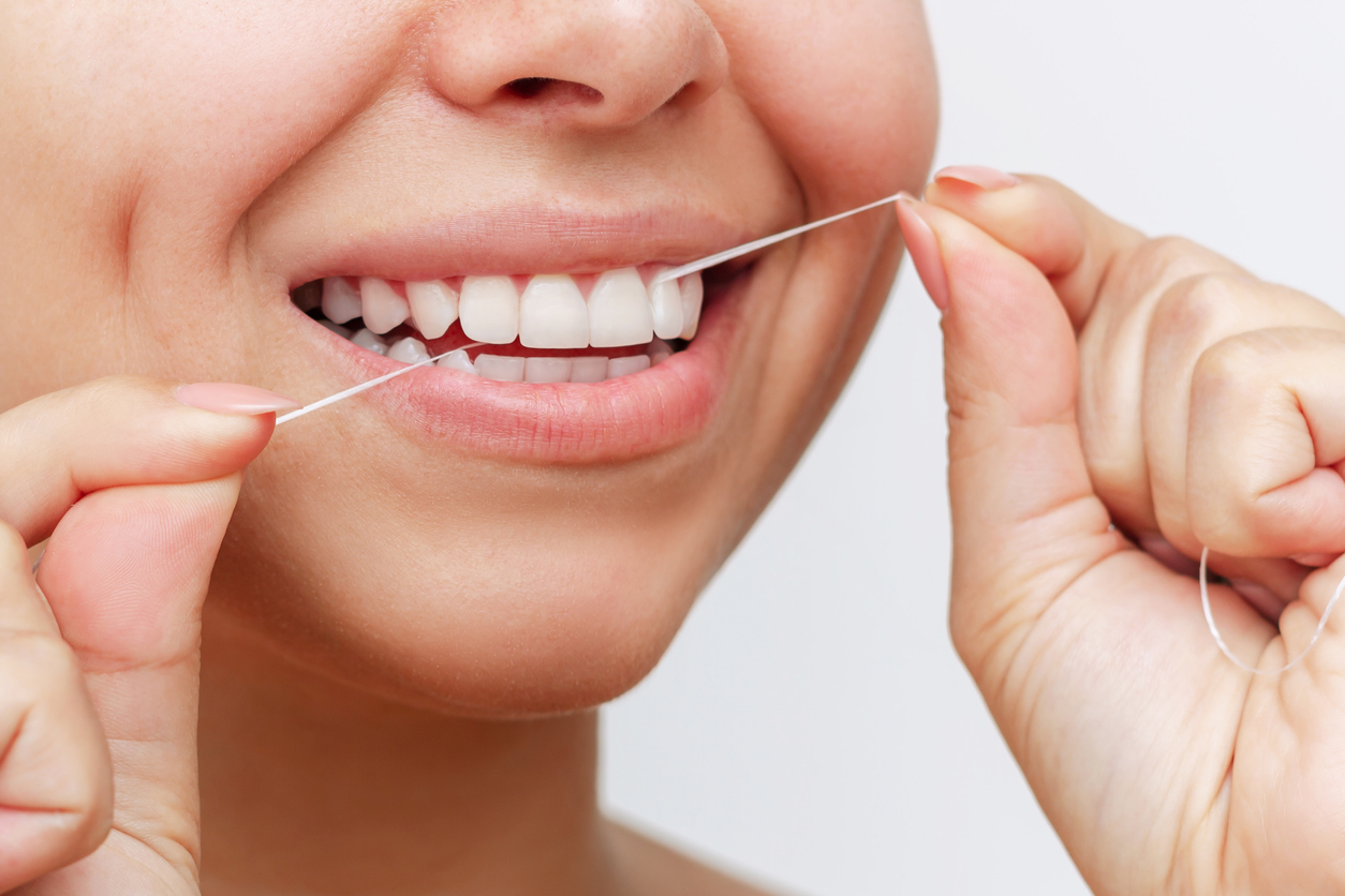 A person smiles as they floss their teeth.